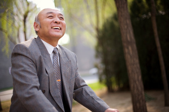 Senior adult businessman riding a bicycle in a park.