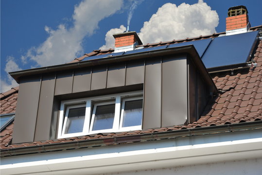 Dachgaube in kupferfarben beschichteter Stehfalz-Metallverkleidung am Ziegeldach eines Wohngebäudes Regenrinne und Regenfallrohr