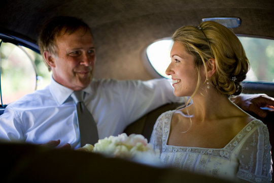 Young adult bride holding flowers in a car with her mature father on her wedding day.