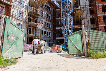 Workers are pouring concrete from cement mixer into wheelbarrow