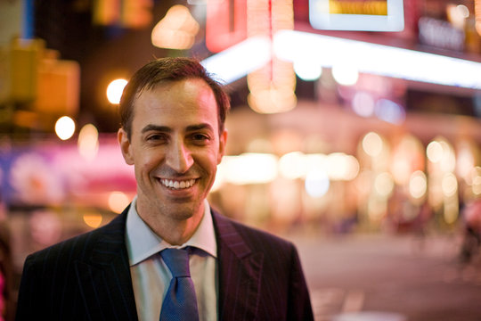 Portrait of a smiling mid-adult businessman at night with city lights behind him.