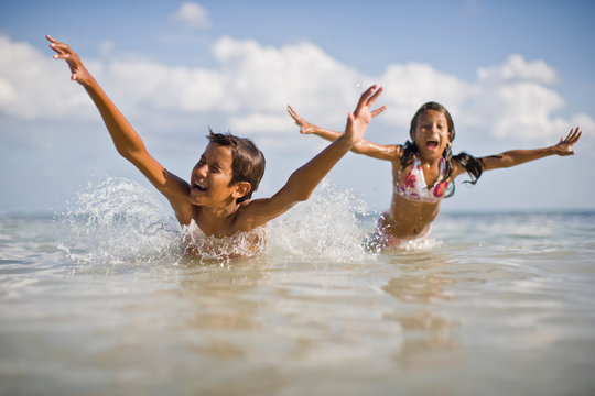 Boy and his younger sister having fun swimming in the water at the beach.