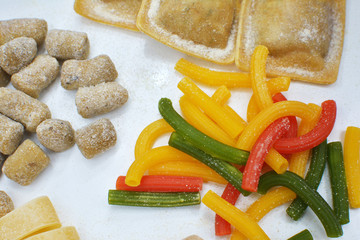 Varietà di pasta fatta in casa cruda fresca colorata con farina su tavolo in legno.