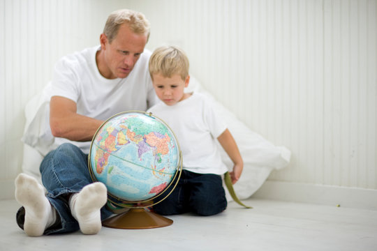 Mid-adult man sitting with his young son looking at a globe.