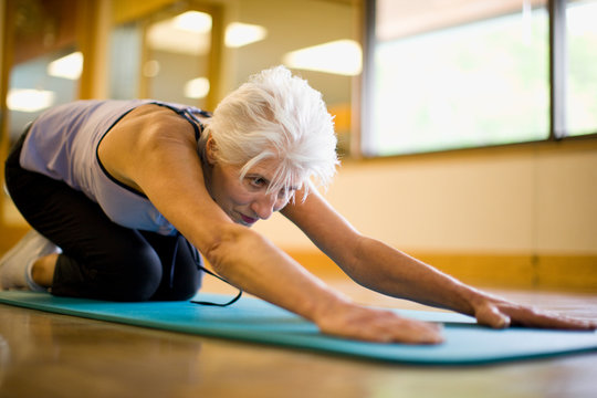 Mature adult woman stretching her lower back at a gym.