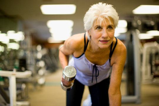 Active senior woman lifting hand weights inside a gym.