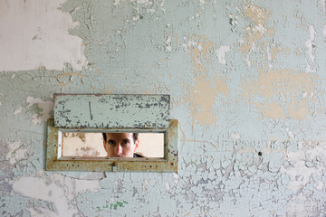 Portrait of a mid-adult businessman peering through a hole in a wall of a derelict building.