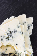 Cheese with mold on a board of stone. Sliced Gorgonzola cheese close-up on the surface of slate.