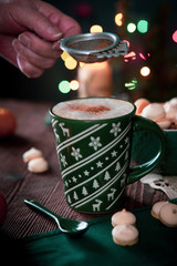 Coffee drink with meringues which pour cinnamon on the background of Christmas lights
