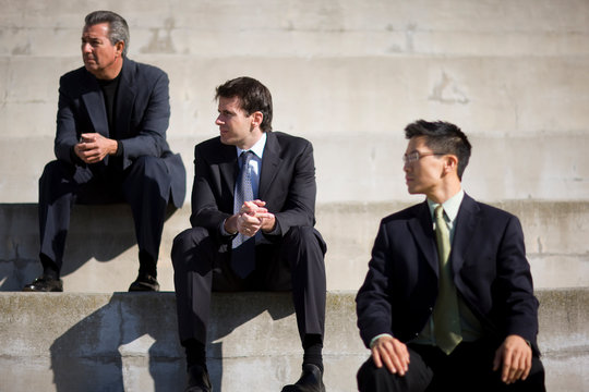 Three businessmen sitting on steps while outside a building.
