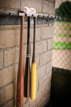 Three baseball bats hanging from a wall rack below two baseballs.