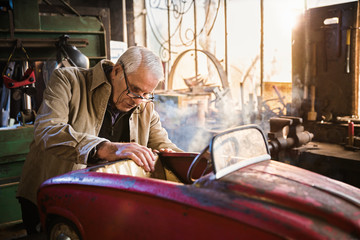 Obraz na płótnie Canvas Senior man in his workshop repairing an old fashioned pedal car 