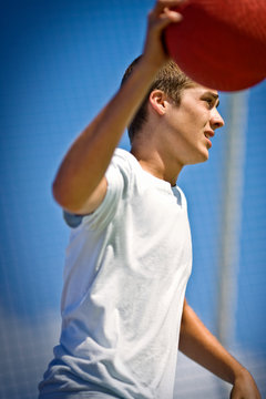 Teenage boy holding a red ball outdoors in the sunshine.