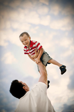Smiling young boy being held aloft by his father.