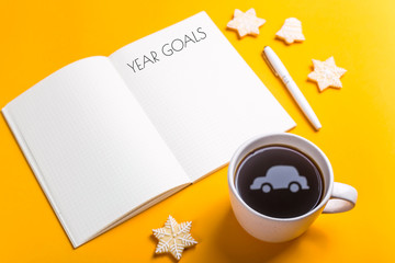 Goals for the year written in a notebook on a yellow background next to a cup of coffee which reflects the shape of the car. Dreams for the new year concept