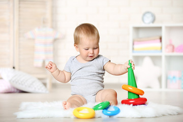 Baby boy with toys sitting on carpet at home