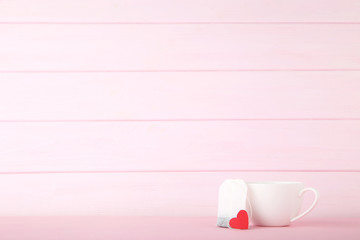 Cup of tea with red heart and teabag on pink background