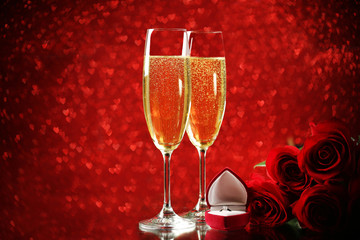 Champagne glasses with red roses and silver rings on lights background