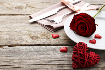Kitchen cutlery with red rose in plate on wooden table