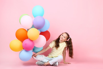 Cute young girl with colored balloons sitting on pink background