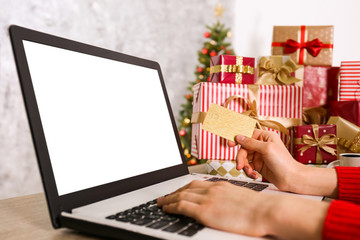 Female hands with golden credit card, laptop, christmas presents, decorated tree on background....