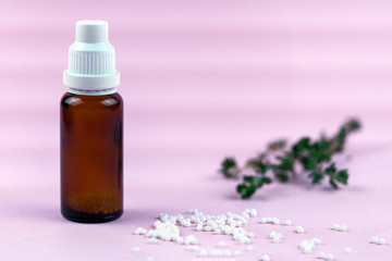Obraz na płótnie Canvas Homeopathic lactose sugar balls in glass bottles ,medicine. Glass bottle with white granules.Close-up of homeopathic globules lying on pink surface with herb and glass bottle.