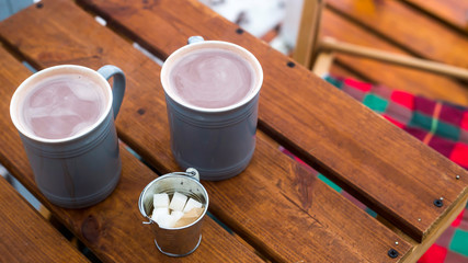 Two cups of cocoa and sugar bucket on a wooden table on the outdoor winter terrace. Hot sweet drink .to warm up on a snowy day