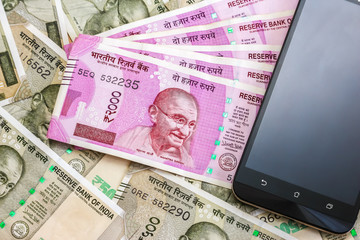 Fototapeta premium Close up view of brand new indian 2000 rupees banknotes and smarthphone. 500 rupee banknotes in background.