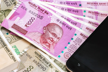 Close up view of brand new indian 2000 rupees banknotes and smarthphone. 500 rupee banknotes in background.