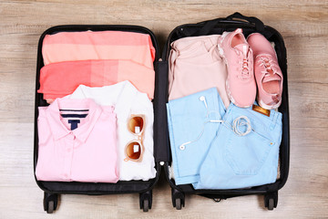 Open suitcase fully packed with folded women's clothing and accessories on the floor. Woman packing...