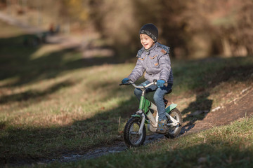 Six years old boy rides bicycle from the hill in the park.
