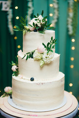 Three-tiered wedding cake with fresh flowers on a green background