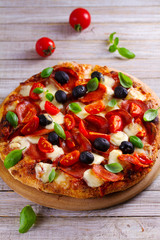 Delicious pizza served on wooden plate. Pizza with pepperoni, tomatoes, cheese, olives and basil