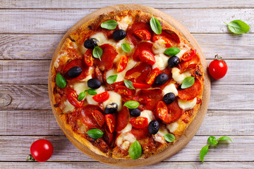 Delicious pizza served on wooden plate. Pizza with pepperoni, tomatoes, cheese, olives and basil. View from above, top studio shot