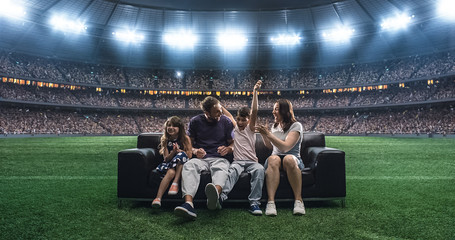 A family is watching a soccer moment, sitting on the couch located in the middle of the soccer...