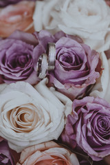 White gold wedding rings on bouquet of purple and white roses