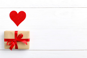 Gift with red ribbon and hearts on white wooden background. Women's or Valentine's Day. Place for text, copy space.