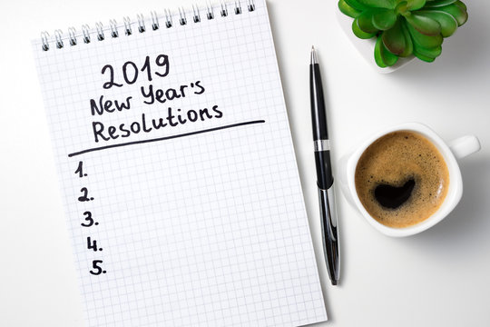 New Year Resolution 2019 On Desk. 2019 Goals List With Notebook, Coffee Cup And Glasses On White Background. Goal, Plan, Strategy, Change, Idea Concept. Top View