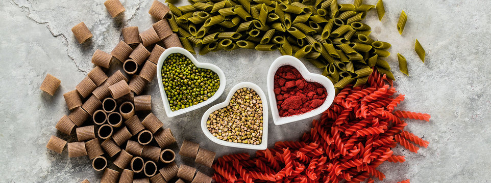 banner of multicolor gluten-free pasta with ingredients in bowls in the form of hearts from which it is made on a stone table