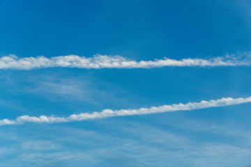 blue sky with line-shaped clouds - contrails of a plane or chemtrails