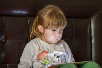 Little girl child plays with tablet pc and is watching