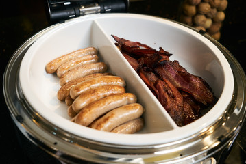 Pork crispy bacon and fried beef sausages in pan on kitchen elec