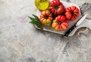brandywine tomato on a cutting board. cooking summer salad with fresh olive oil, thyme. on a stone table
