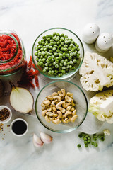 fresh ingredients for a gluten-free red lentil pasta with cauliflower and green peas with olive oil and spices on the marble table . healthy vegan cuisine
