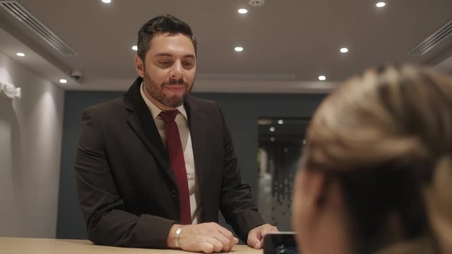 Happy business man arriving at corporation reception desk for meeting with client, financial consultant in corporate office to meet businessman. Manager talking to woman at work as receptionist