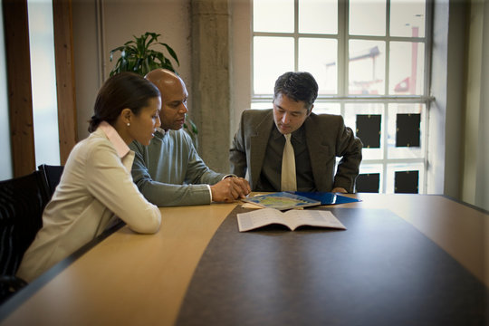 Three business colleagues sitting at a table during a meeting inside a boardroom.