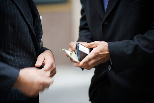 Businessmen opening his wallet while standing next to a colleague.