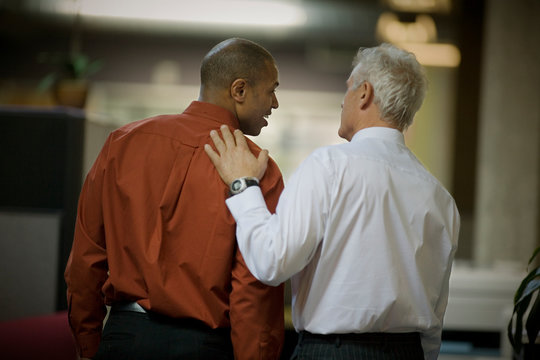 Mature adult businessman patting a mid-adult male colleague on the back.