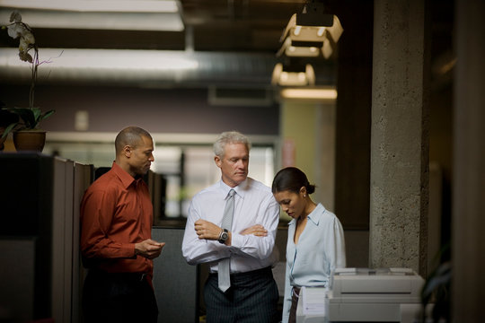 Mid-adult business woman talking with two male colleagues in an office.