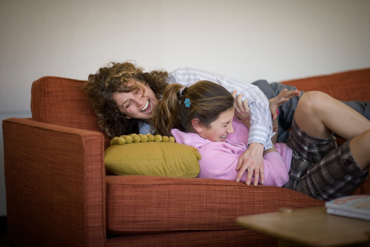 Mid-adult business woman hugging her teenage daughter on a couch.